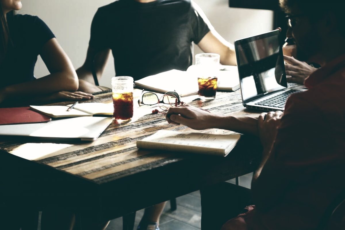 Profissionais reunidos à mesa de trabalho, com documentos e laptops